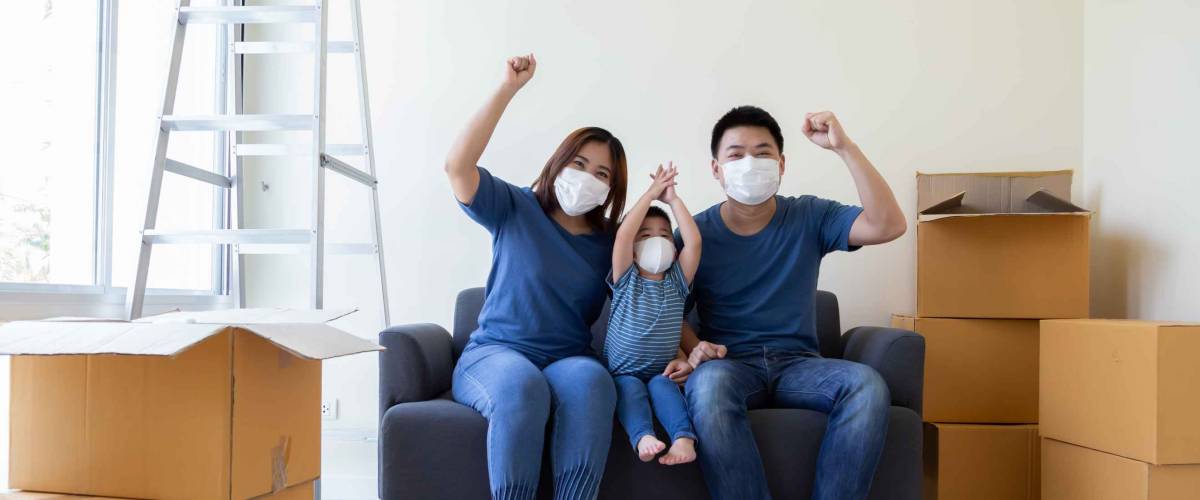 Asian family wearing protective medical mask for prevent virus covid-19 and hand up during moving day and relocating at new home. Moving house and new real estate concept
