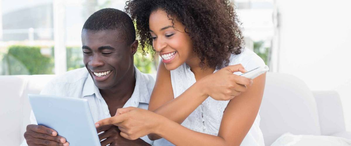 Attractive couple sitting on couch together looking at tablet at home in the living room