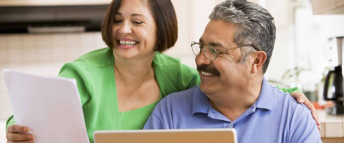 Couple in kitchen with laptop and paperwork smiling