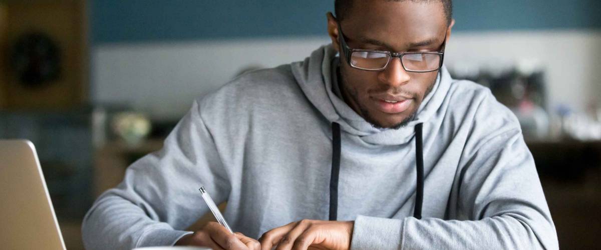 Focused millennial african american student in glasses making notes