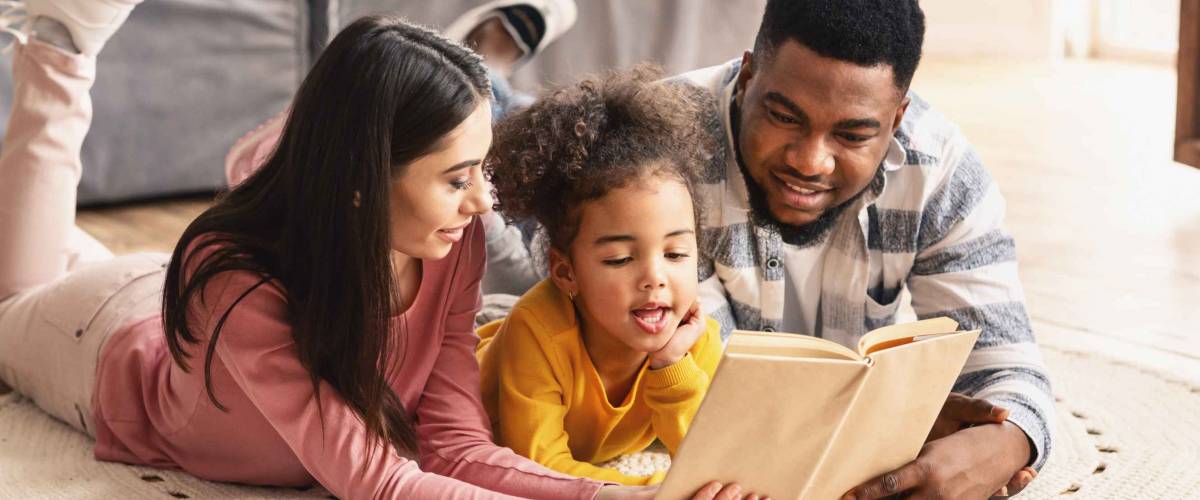 International millennial family reading book on the floor at home