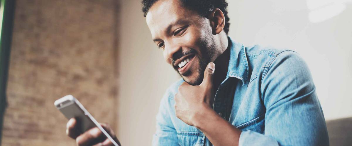 Happy bearded businessman using phone while sitting on sofa
