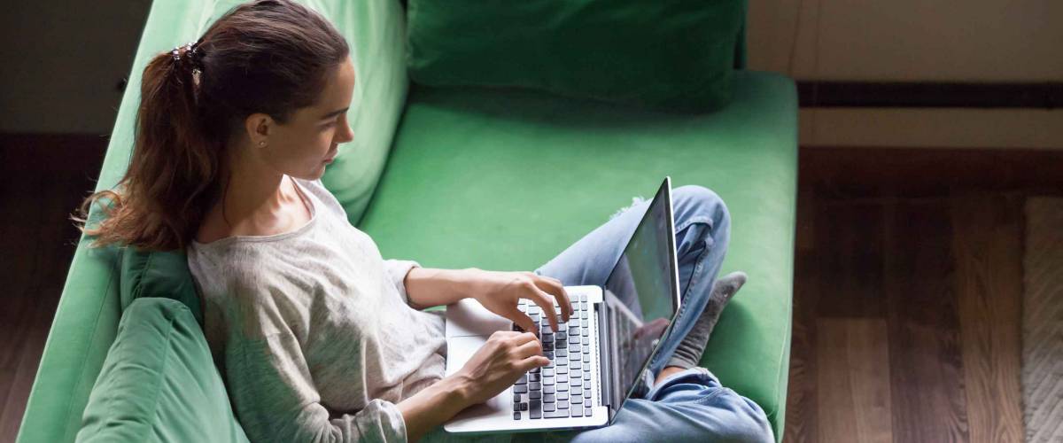 Relaxed woman using laptop sitting on sofa, doing online shopping