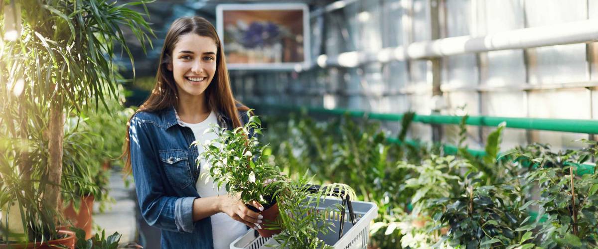 Portrait of young female shopper walking through indoor garden store looking at camera smiling.