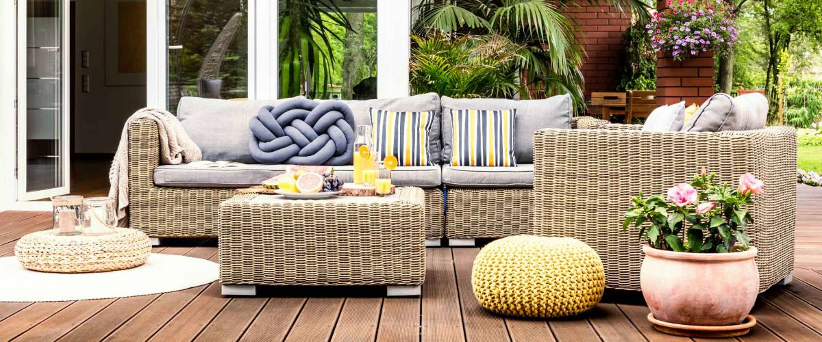 Beige garden furniture with striped pillows on a wooden terrace with pink flowers and poufs