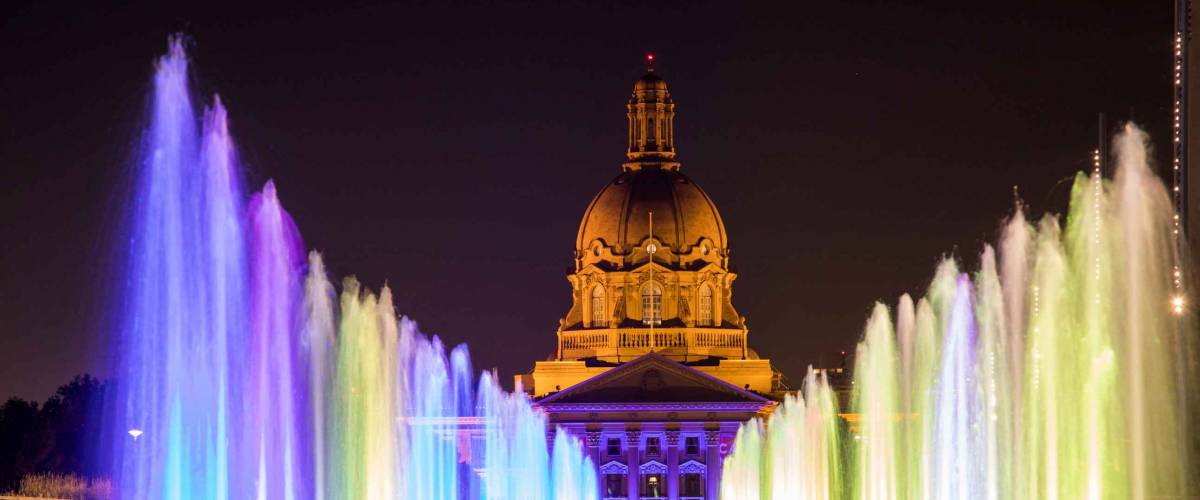 Colorful fountains illuminate a plaza in Downtown Edmonton, Canada, with Alberta's Legislature Building in the background.