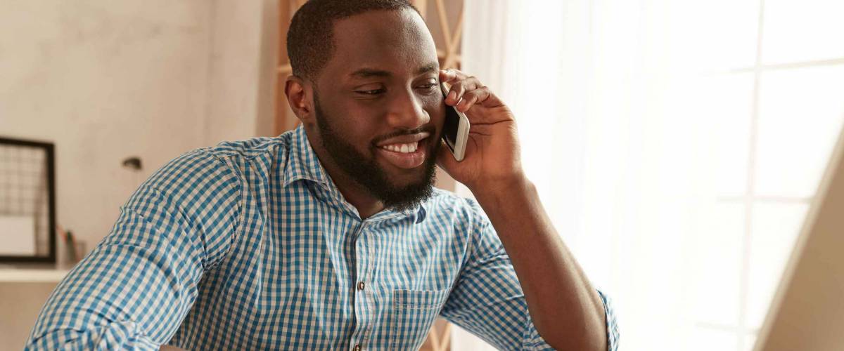 Good news. Happy Black businessman in shirt talking by phone and smiling while at home