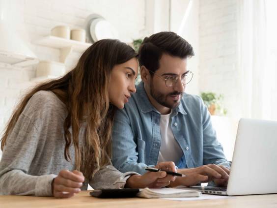 Focused young couple calculating bills, discussing planning budget together, serious wife and husband looking at laptop screen, using online banking services and calculator, checking finances