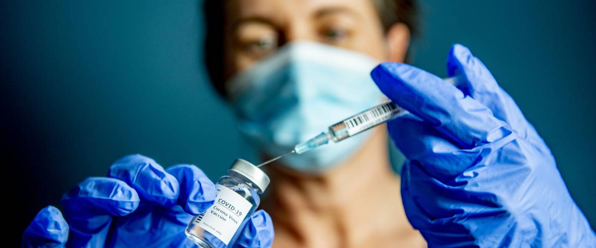 Woman holding a syringe and vaccine wearing rubber gloves