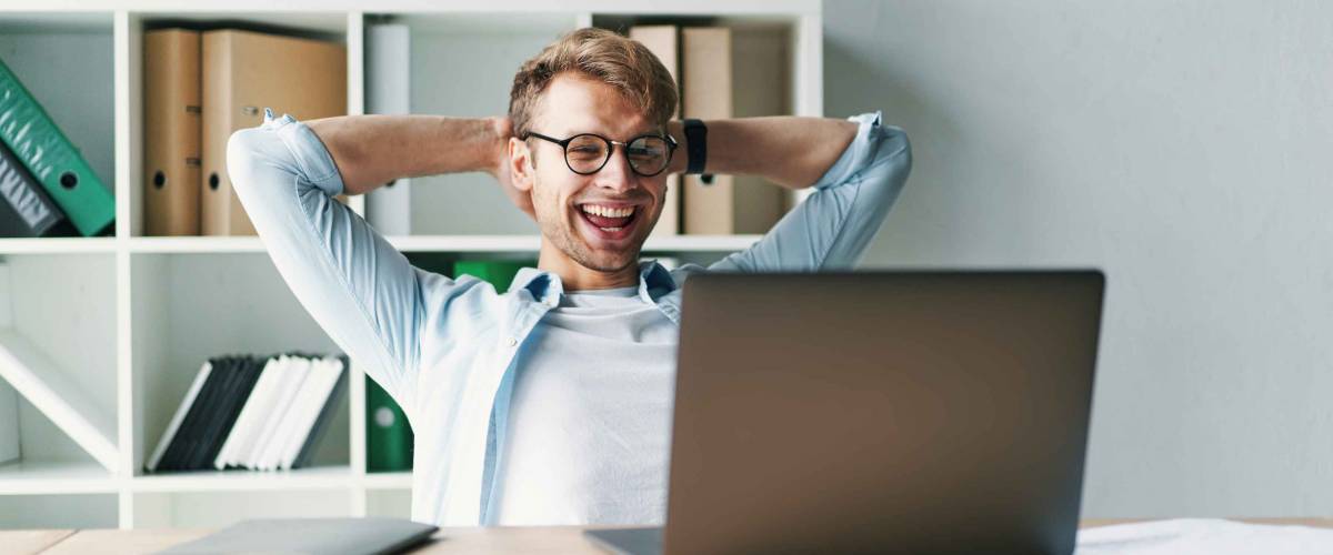 Young man smiling as he reads the screen of a laptop computer while relaxing working on a comfortable place by the wooden table at home. Happy Social distancing