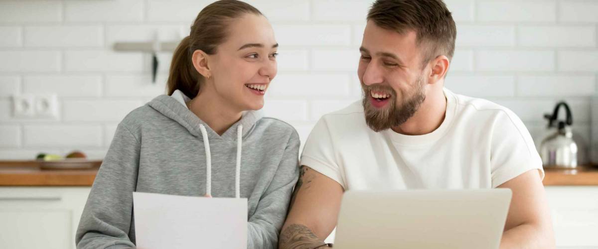 Young smiling happy couple talking at home in the kitchen with laptop