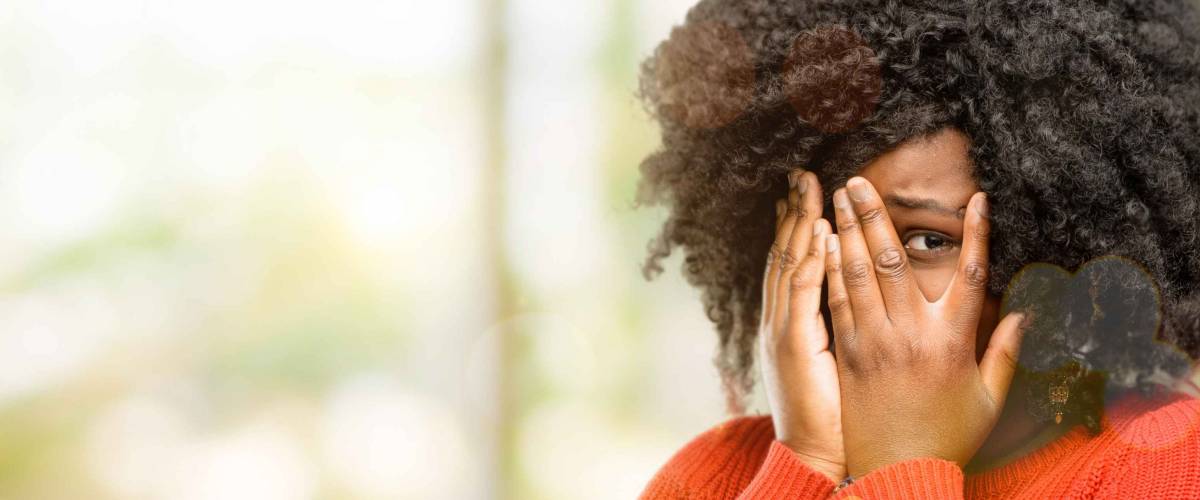 Beautiful african woman smiling having shy look peeking through her fingers, covering face with hands looking confusedly broadly, outdoor