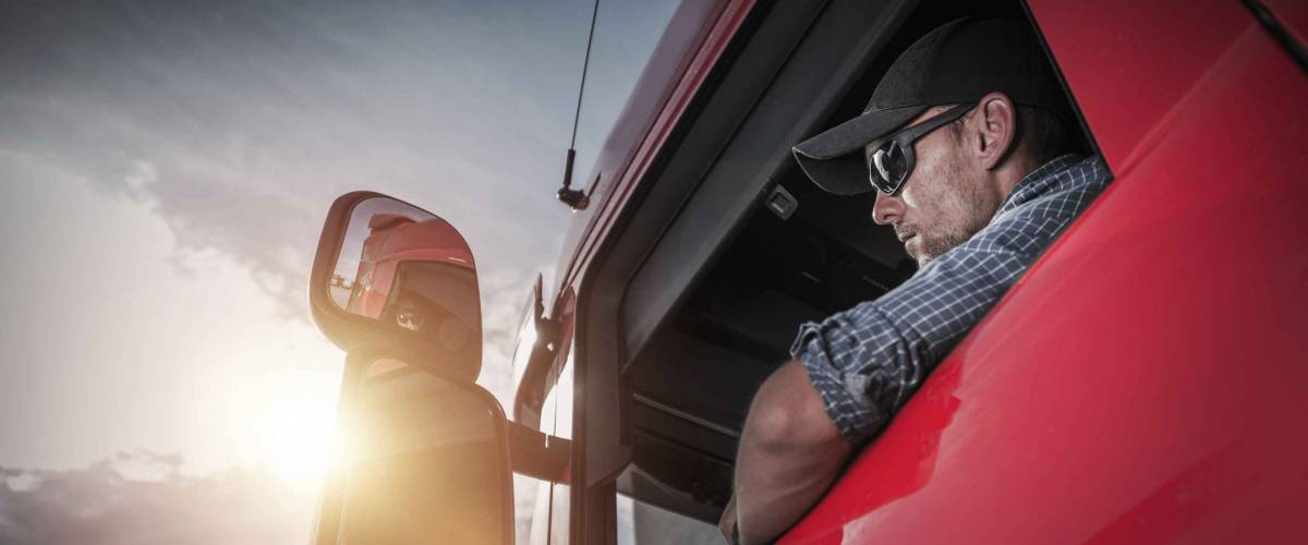 Man driving a red truck wearing glasses and a hat