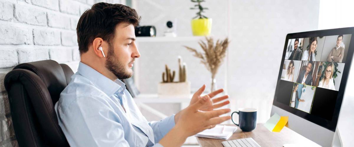 Man sitting at desk talking with hand to screen with co-workers on video chat