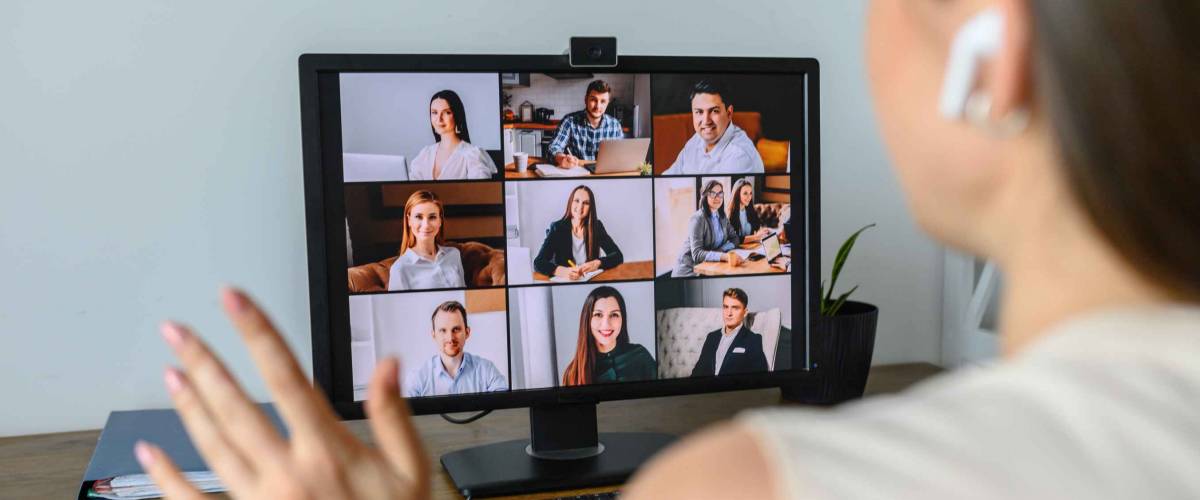 Morning meeting online. A young woman is using app on pc for connection with colleagues, employees. Video call with many people together. Back view