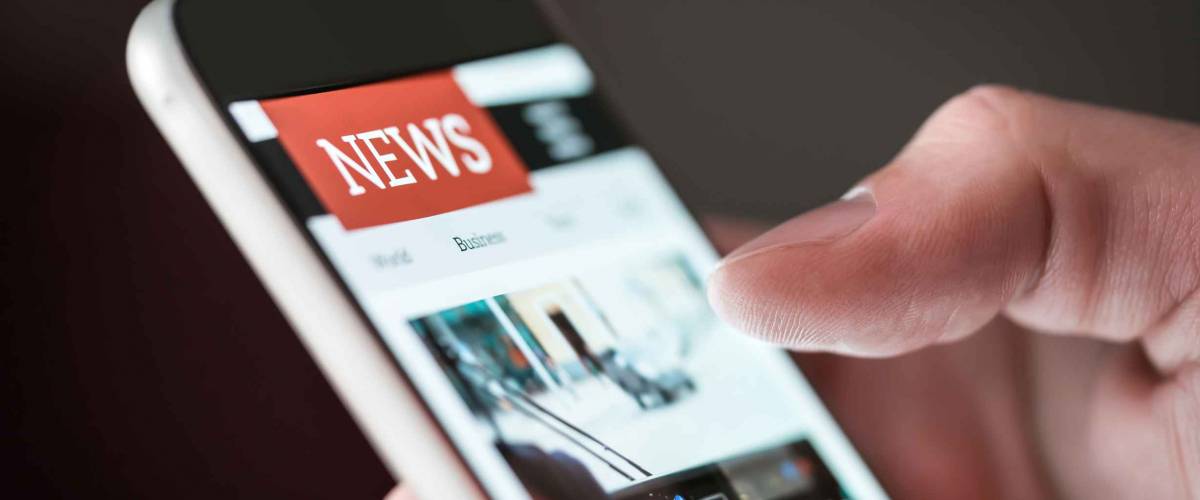 Mobile news application in smartphone. Man reading online news on website with cellphone. Person browsing latest articles on the internet. Light from phone screen.