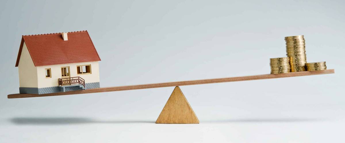 Model house and money coins balancing on a seesaw