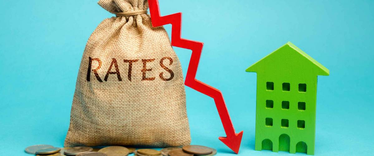 Money bag with the word Rates, down arrow and wooden house. The concept of reducing interest rates on mortgages. Low rental rate for housing. Real estate market and loan.