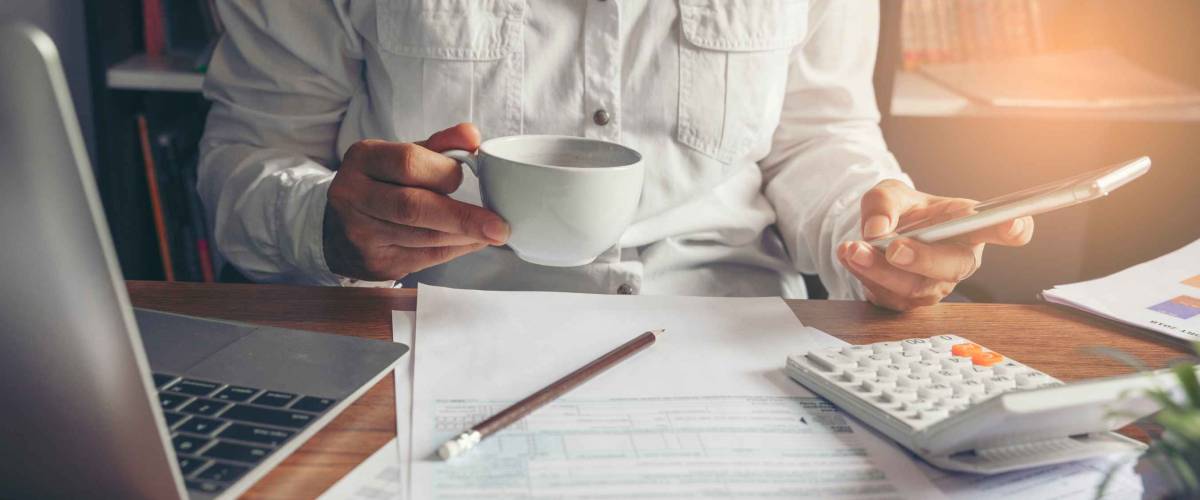 Budget planning concept. Accountant using smartphone calculating return tax. Calendar 2021 and personal income annual tax forms for those who have income under US law placed on office desk.