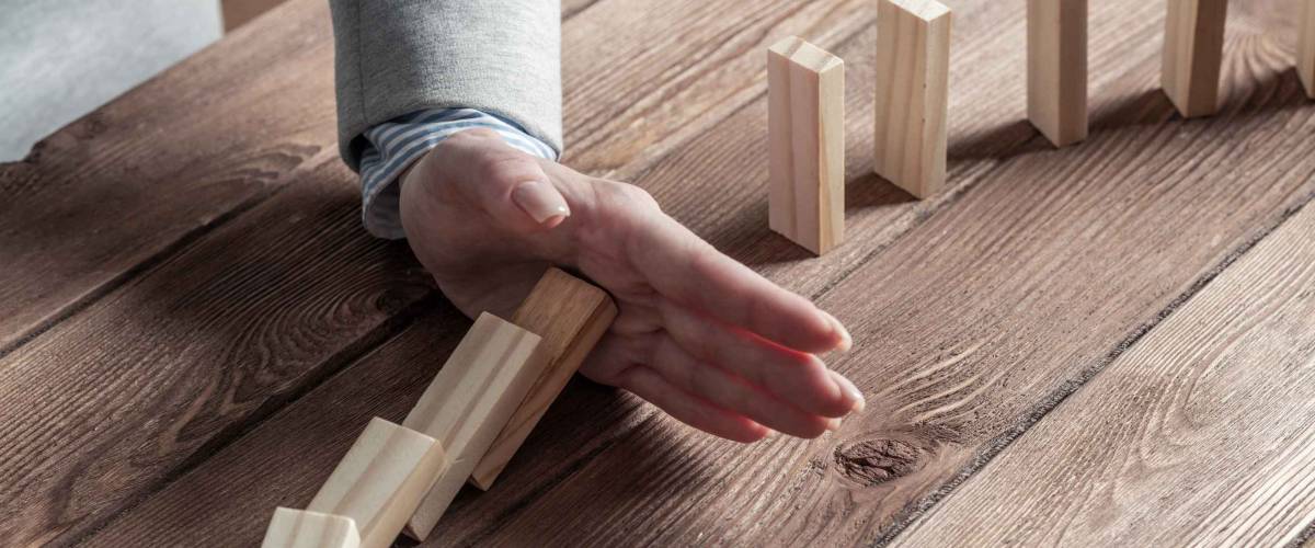 Businesswoman protecting dominoes from falling on wooden desk. Business assistance and leadership in crisis. Operative business solution and stabilization of situation.