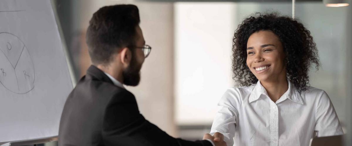 Happy millennial african American businesswoman shake hand greeting or get acquainted with male colleague, smiling biracial woman employee handshake man partner, closing deal at negotiations