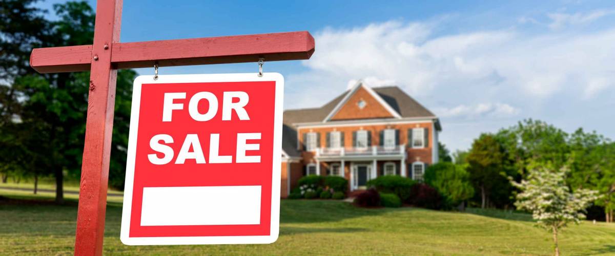 For Sale realtor sign in front of large brick single family house in expansive grass yard for real estate opportunity