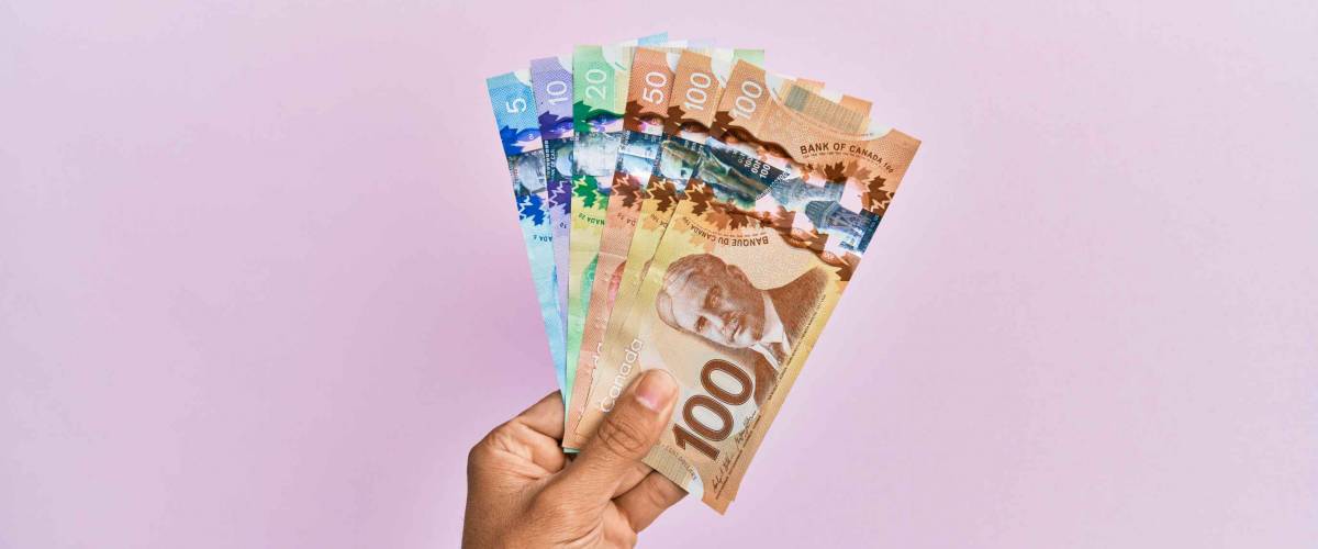 Hispanic hand holding canadian dollars banknotes over isolated pink background.
