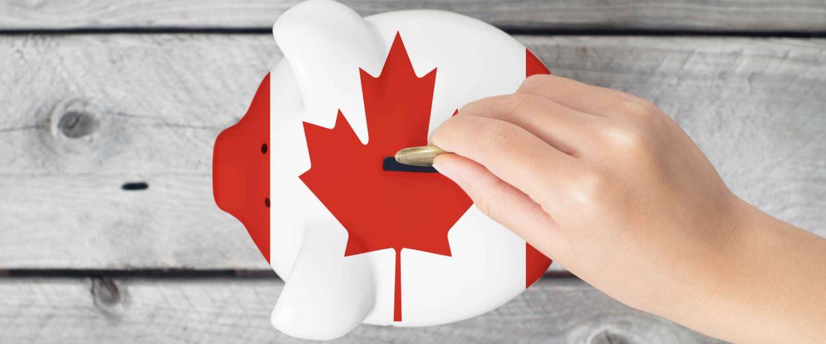 Canada saving concept with little hand dropping a coin into piggy bank overlaid with Canadian flag