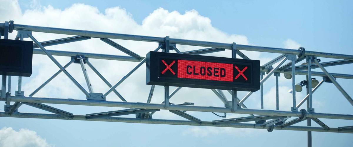 LED closed sign at country border gate against blue sky. Border closed in coronavirus pandemic lockdown to restrict non-essential travel.