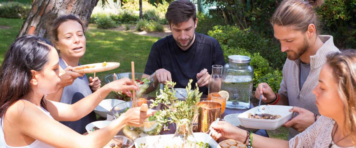 Portrait of serious young people having lunch outdoors. Friends sitting at table and eating together in garden. Outdoor party concept