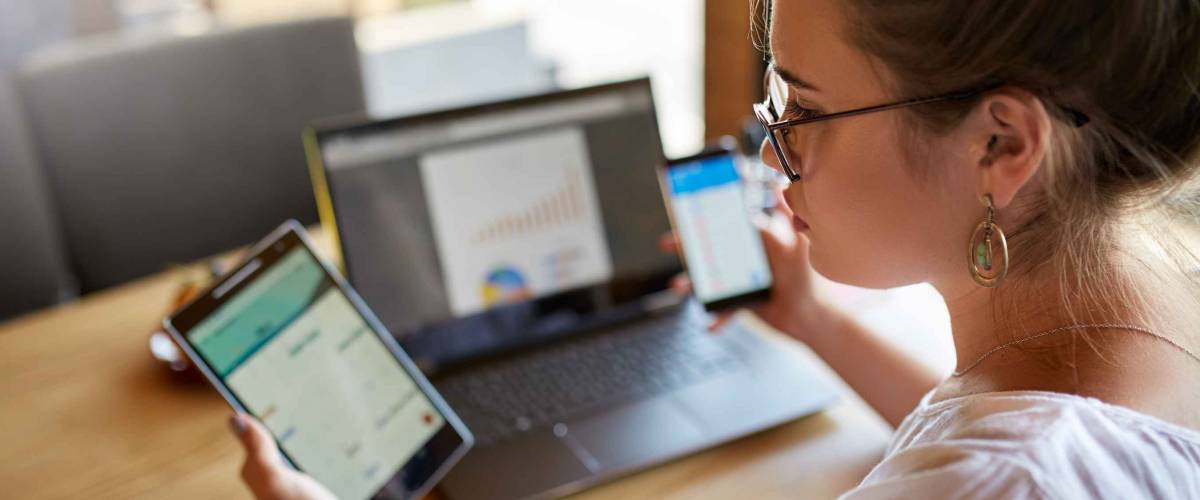 Mixed race woman in glasses working with multiple electronic internet devices.