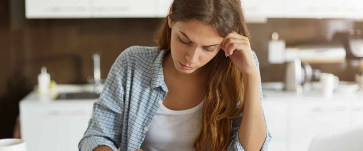 Young woman looking down at a stack of bills, looking concerned.