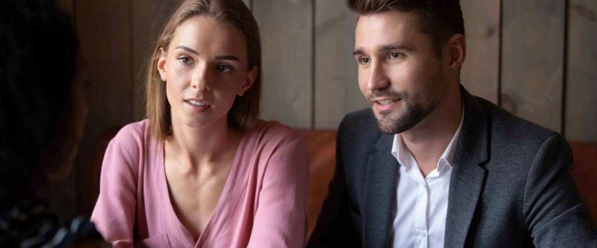 Focused Caucasian husband and wife talk discuss buying house with female real estate agent in coffeehouse, concentrated couple meeting with wedding planner or financial consultant in cafe