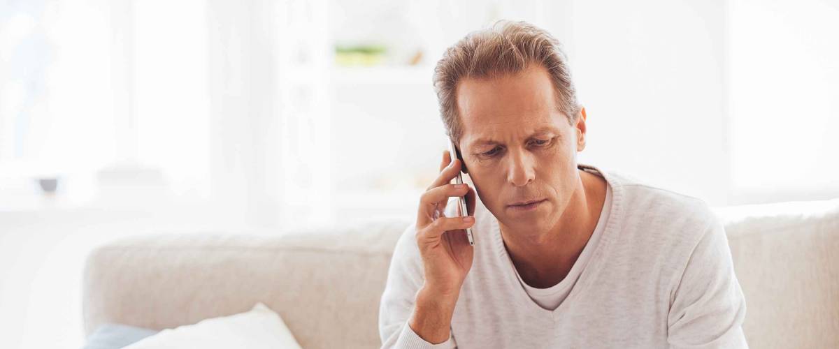Discussing that document. Serious mature man holding paper and talking on the mobile phone while sitting on the couch at home