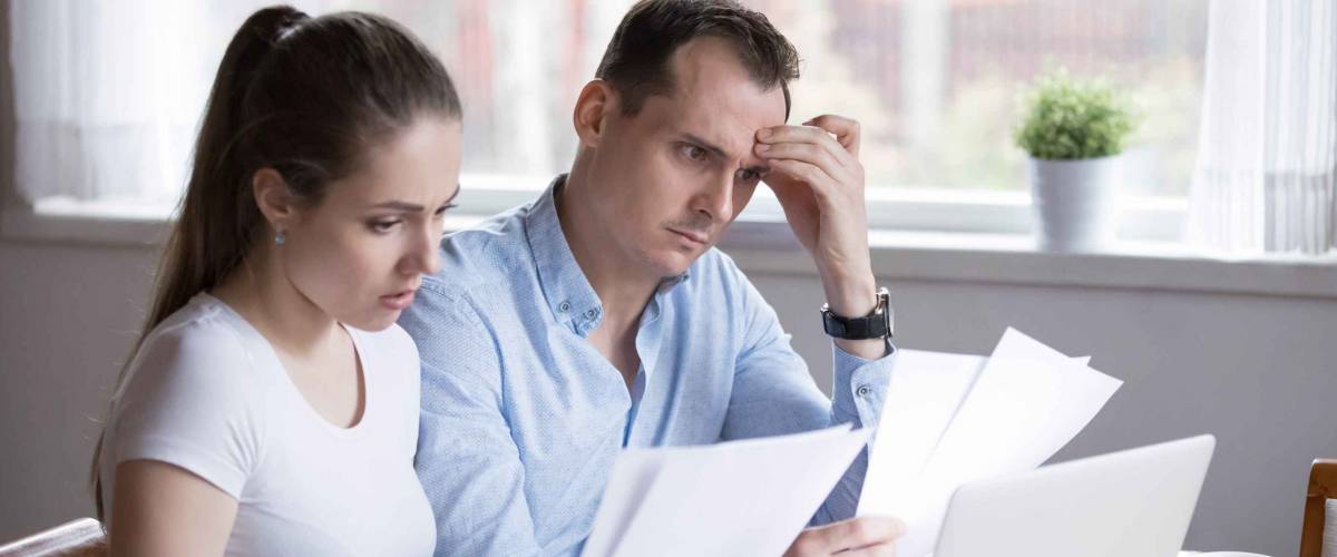 Serious couple looking at sheets of paper, looking concerned at kitchen table