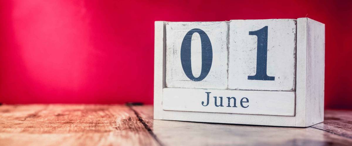 June 1st. Day 1 of month, calendar on business office table, workplace with vivid maroon red background. Summer time