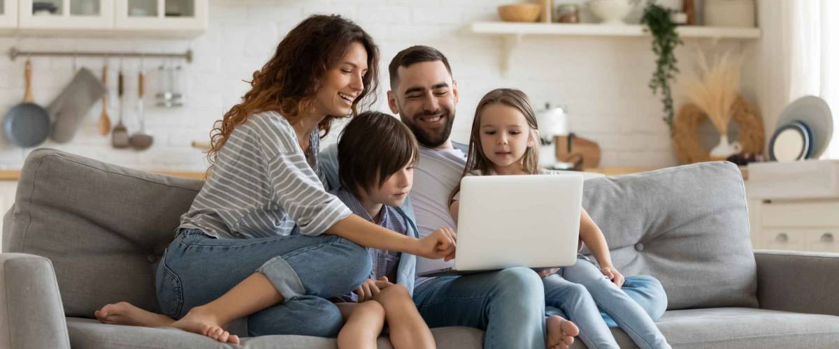 Happy young family with little kids sit on sofa using laptop