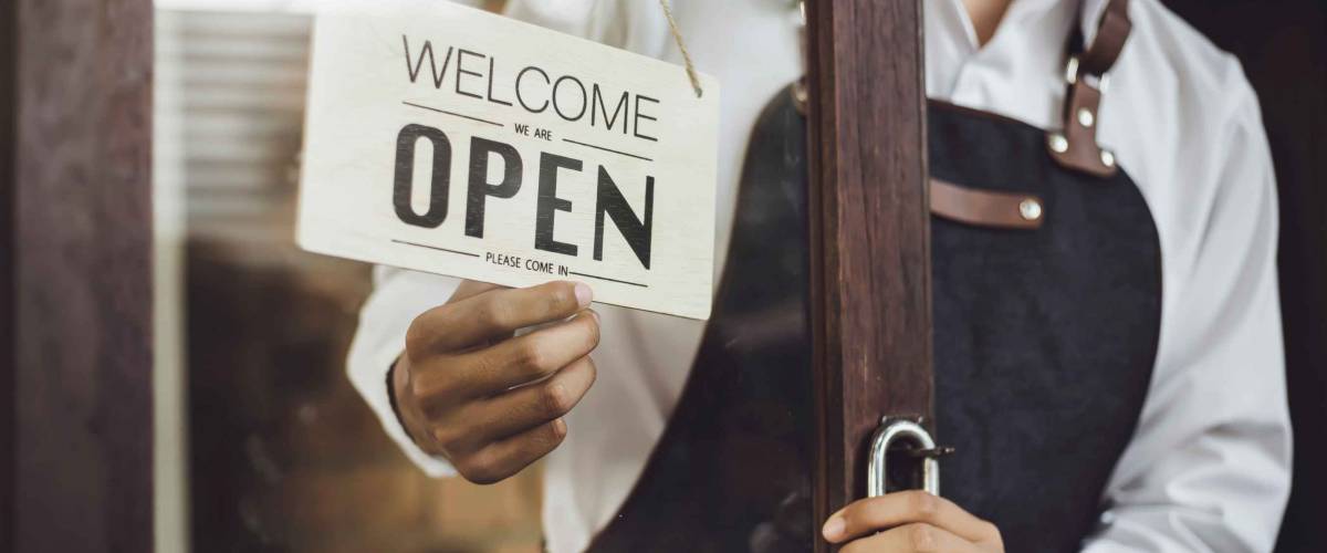 Store owner turning open sign broad through the door glass and ready to service.