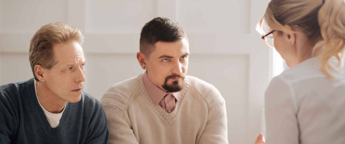 Serious anxious gay couple listening to financial adviser.