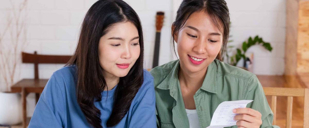 Two women do budget planning at dining room table, looking at receipts.
