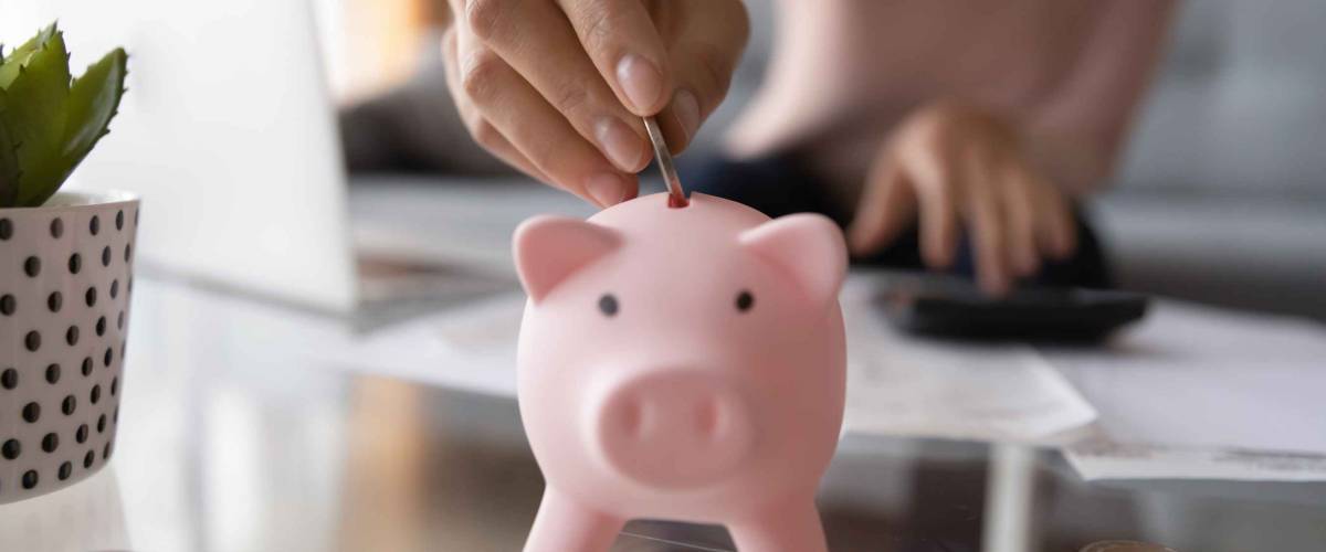 Close up young person putting coin in piggy bank.