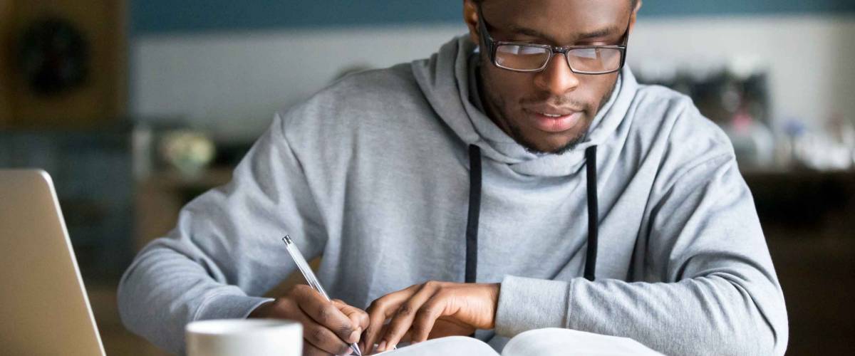 Focused millennial african american student in glasses making notes