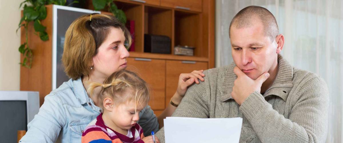 Upset parents discussing sheet of paper at kitchen table.