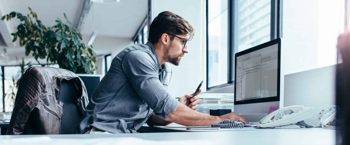 Young man sitting in office and working on desktop pc. Businessman looking at computer monitor while working in office.