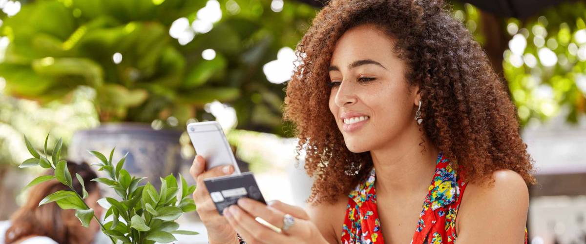 Young woman sits at cafe with phone and credit card in her hands.
