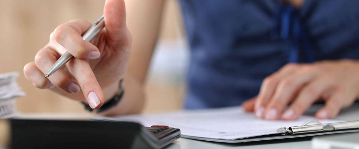 Close up of woman using calculator, writing notes.