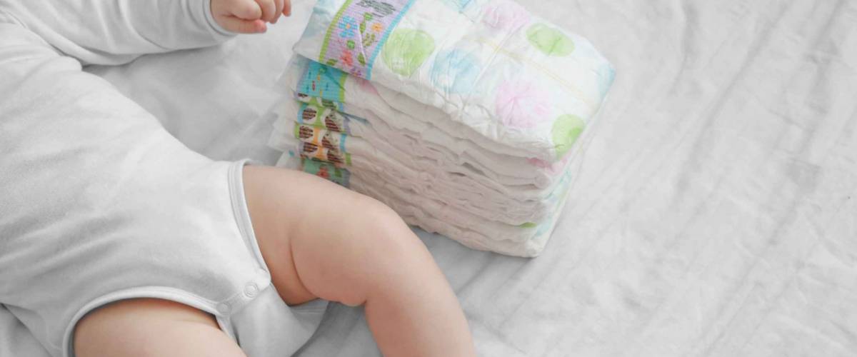 Baby feet and a pack of diapers on a white bed.
