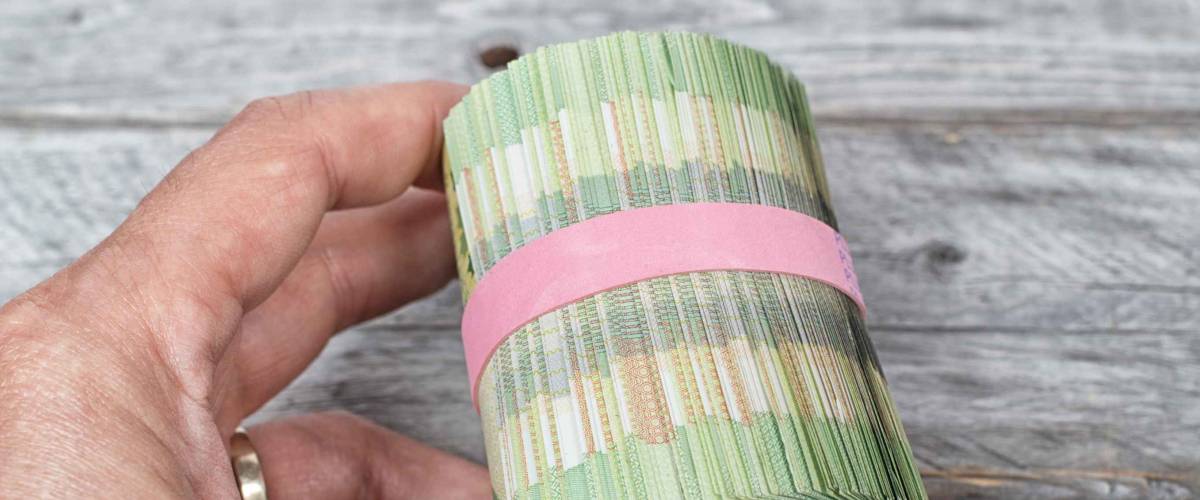 Hand holding a roll full of green bank notes against a wooden background