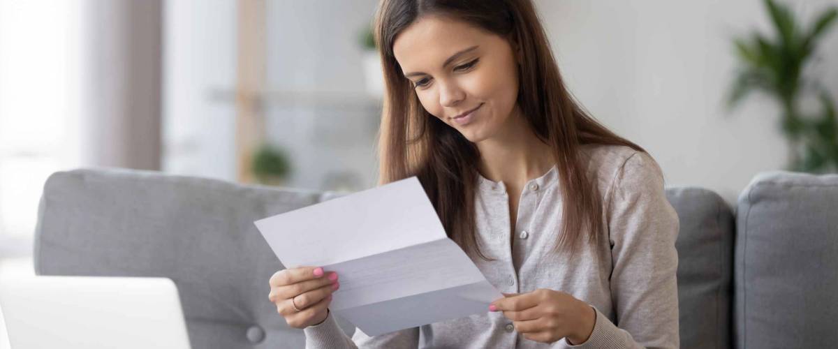 Young attractive woman sitting on sofa at home holds paper reading letter