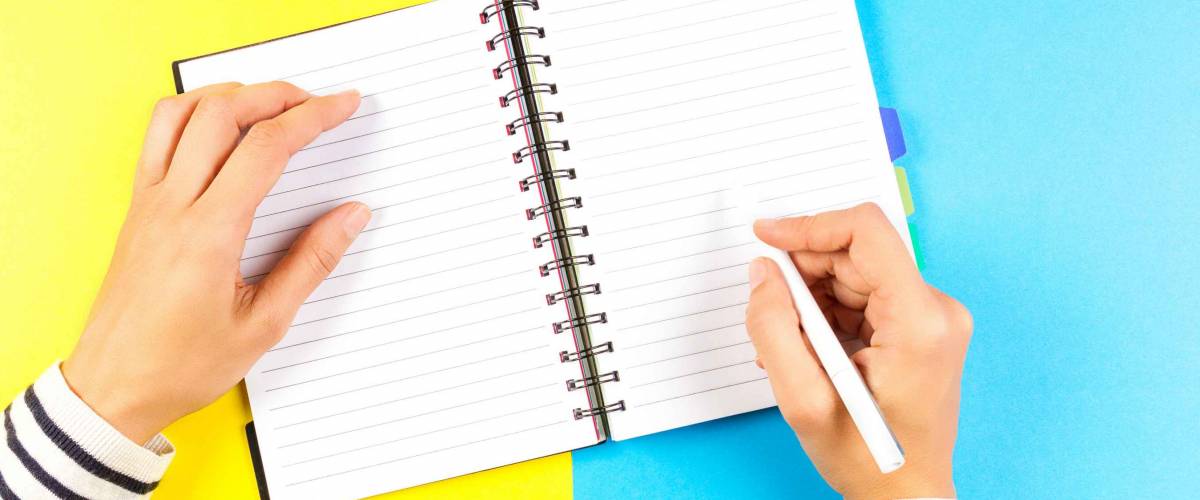 Woman hand writing in notebook over blue and yellow background.